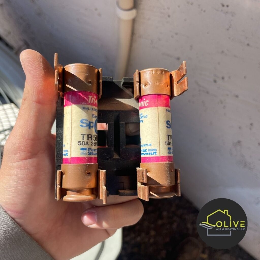 A close-up image of a technician holding two burnt-out fuses, highlighting the importance of regular heating system inspections to prevent breakdowns and ensure safety. Heating Repair